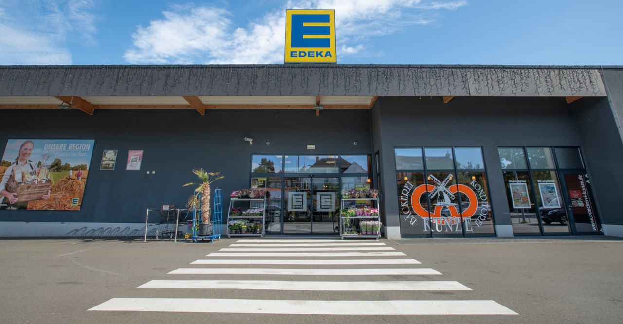 Gebäude mit Zebrastreifen davor und dem gelb-blauen EDEKA-Logo auf dem Dach.