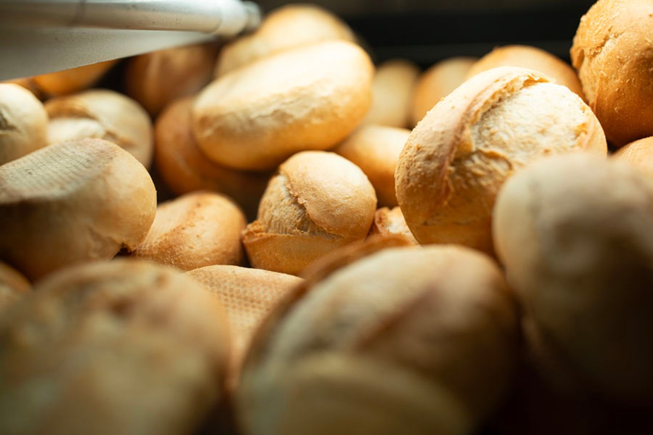 Haufenweise frisch gebackene, goldbraune Brötchen mit knuspriger Kruste, einige im Vordergrund unscharf.