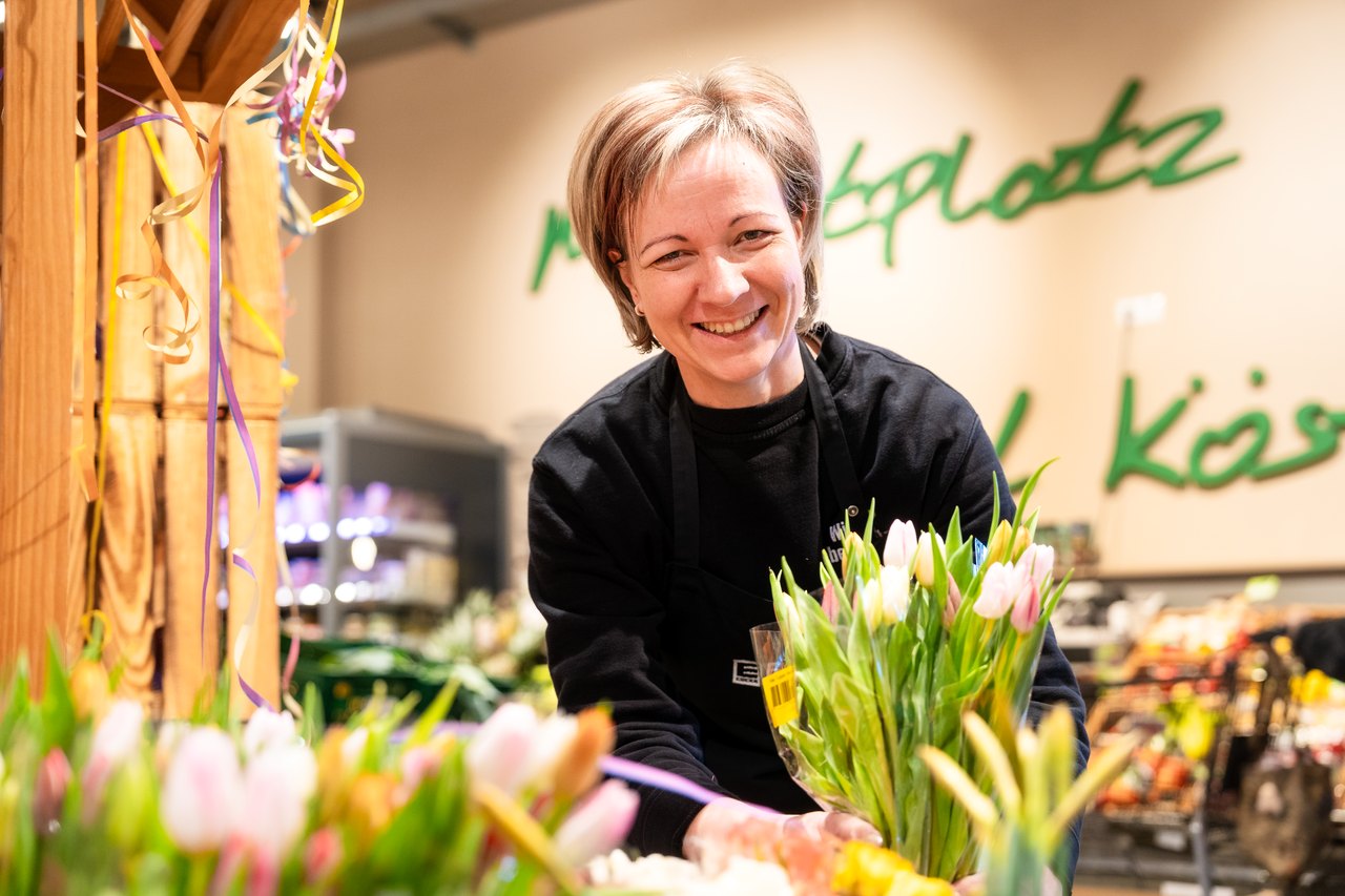 Lachende Floristin in schwarzem Oberteil bindet einen Strauß bunter Tulpen im Blumenladen.